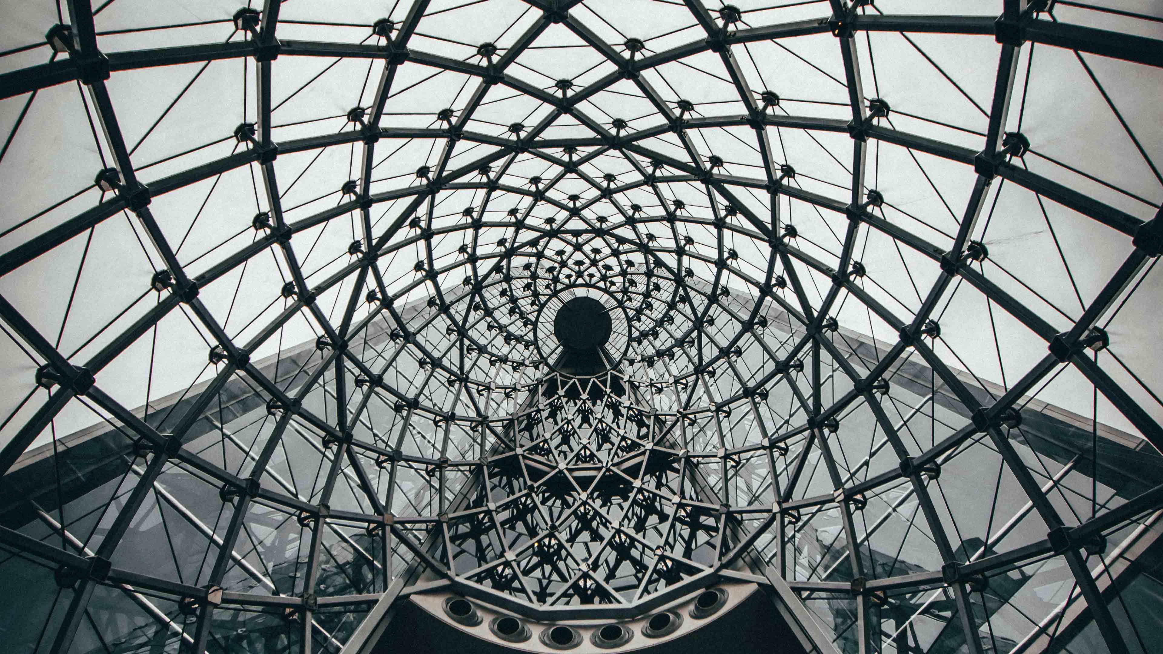 Intricate geometric glass and metal structure forming a spiral pattern inside a modern building.