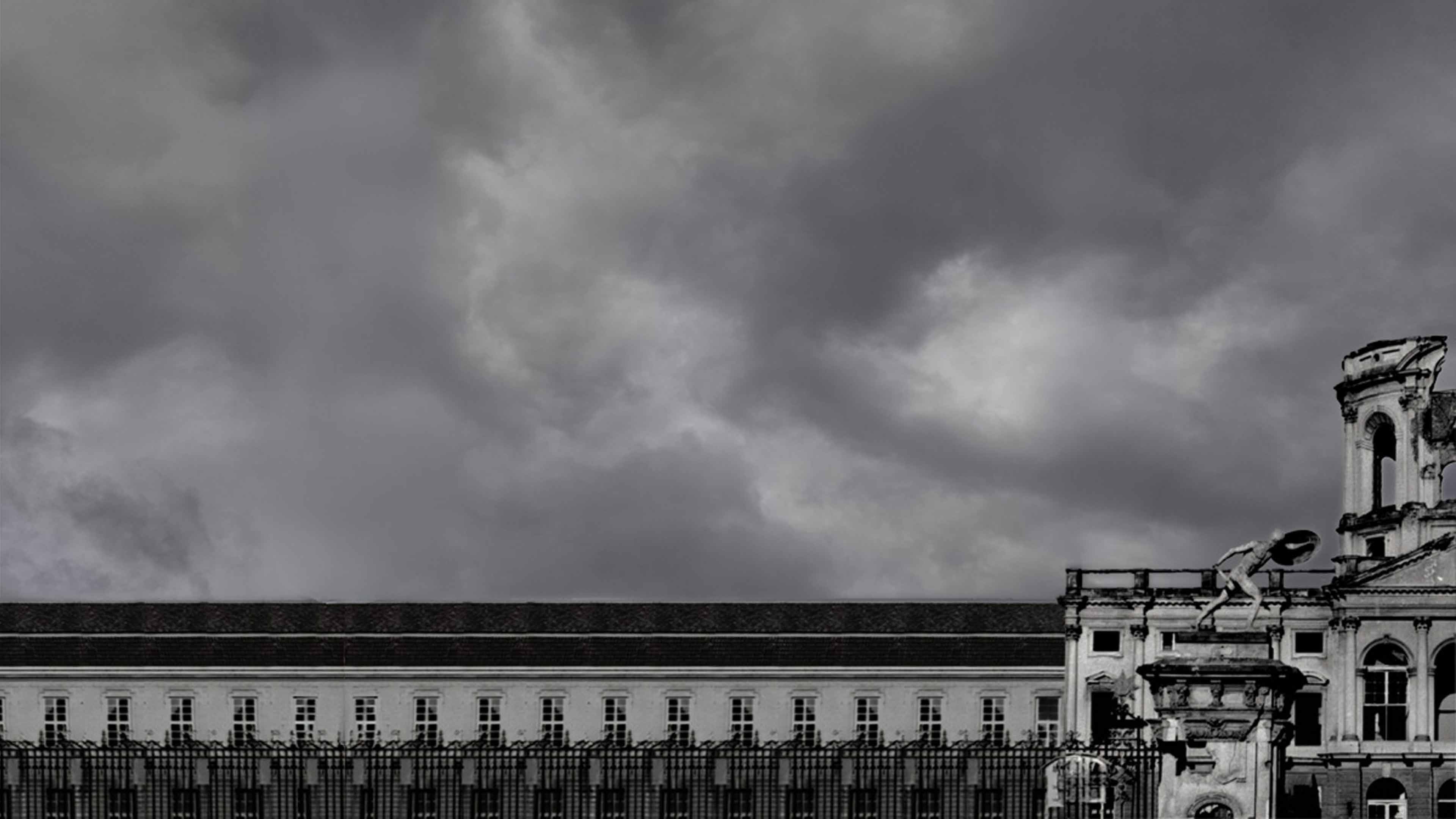Historic building with statue atop stone pedestal under a cloudy, dark sky in black and white.