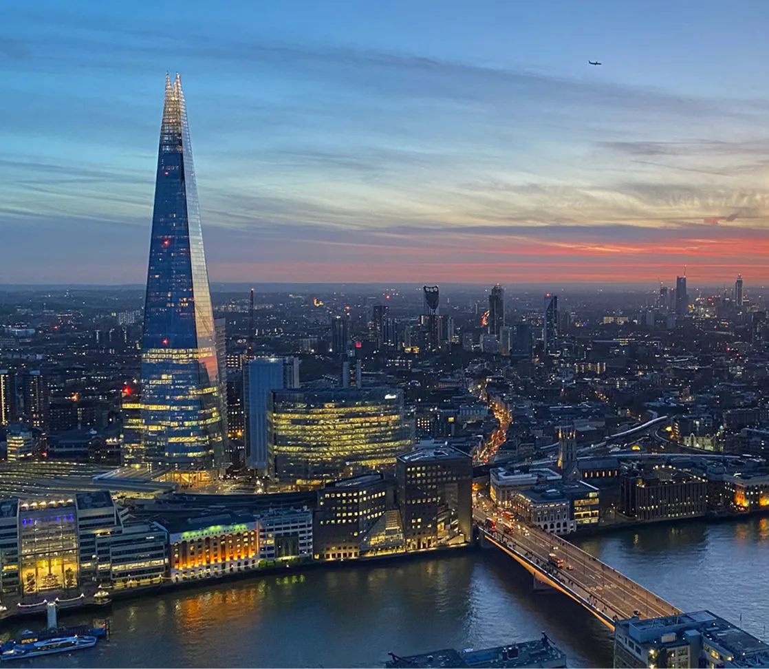 Evening cityscape of London featuring The Shard and a bridge over the River Thames at sunset.