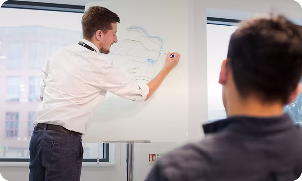 Man writing on a whiteboard during a meeting with a colleague watching in a modern office.