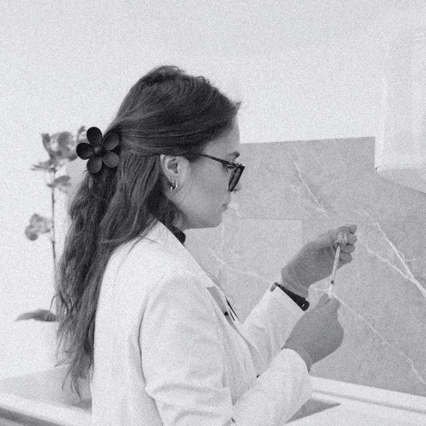 Mujer con bata blanca y gafas prepara una jeringa en un entorno clínico.