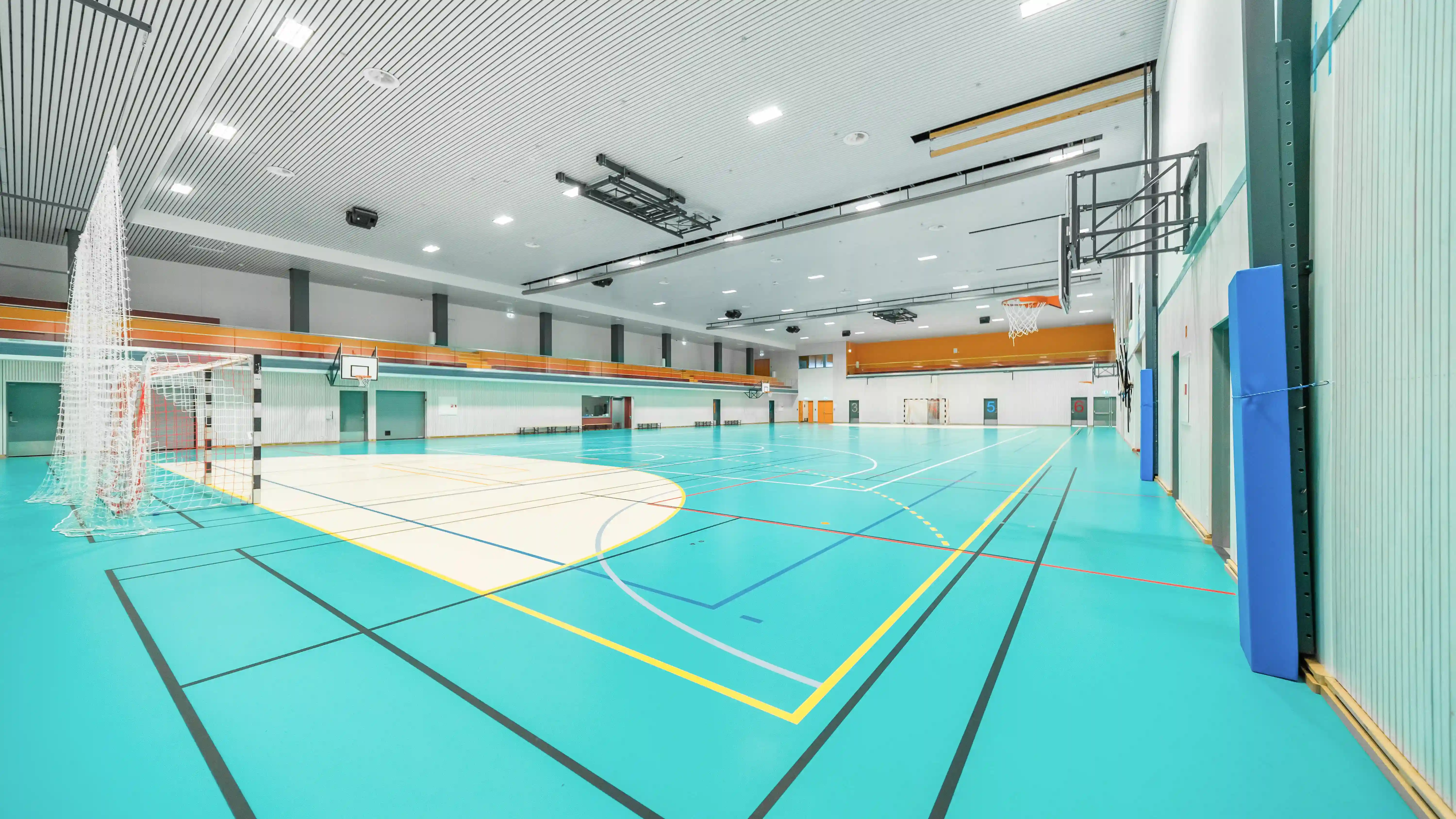 Tømt innendørs idrettshall med turkis gulv, basketballkurver og håndballmål.