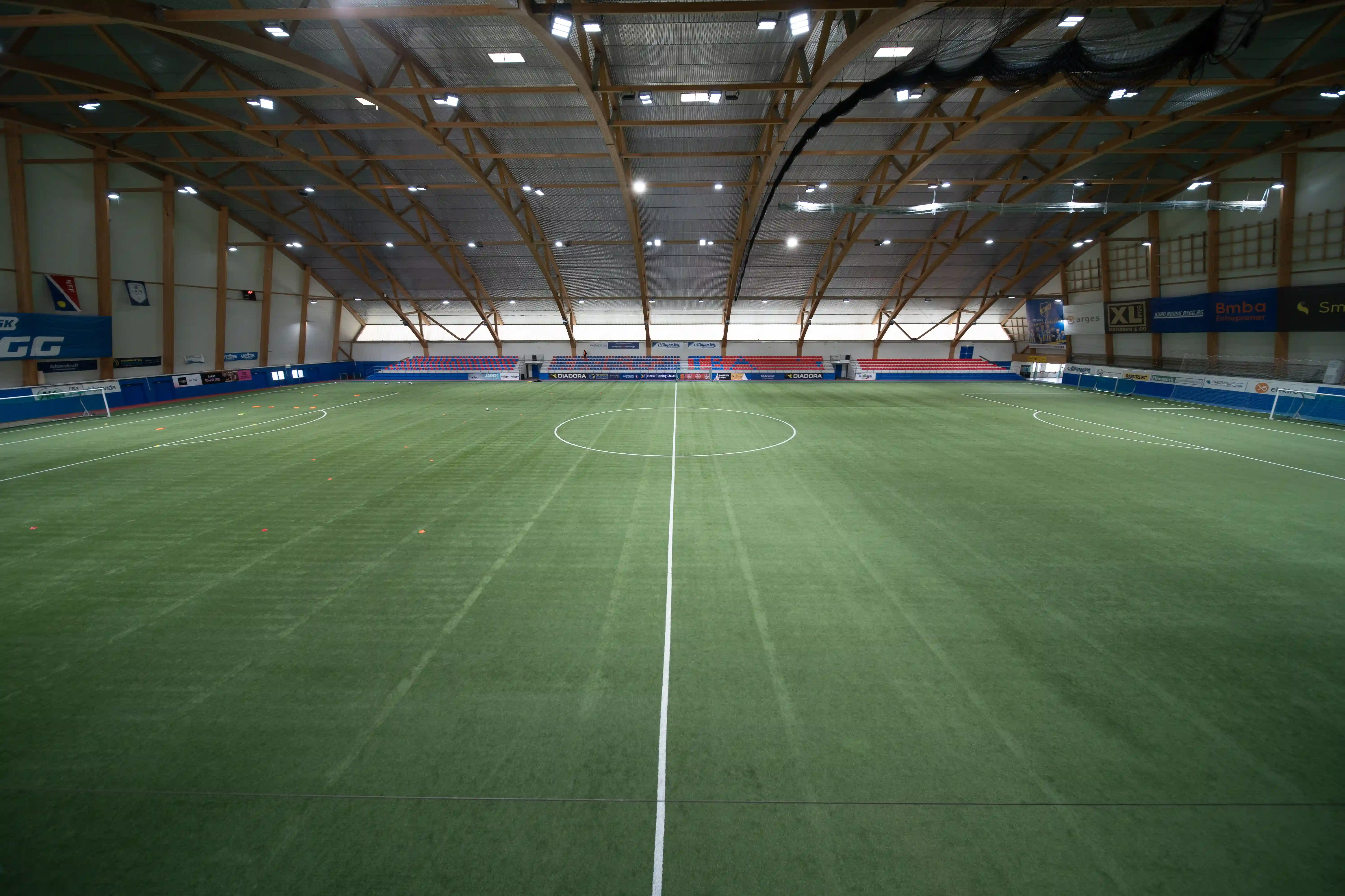 Innendørs fotballbane med gress, tribuner og trestøttestruktur i taket.