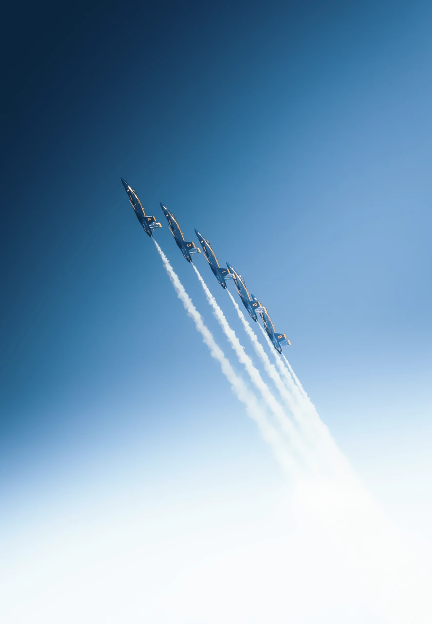 Cinq avions de chasse en formation en montée avec des traînées blanches dans un ciel bleu clair.