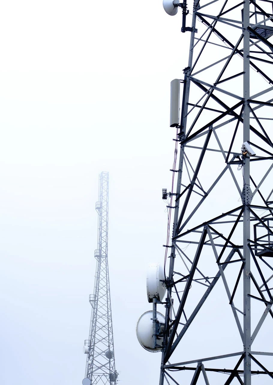 Deux tours de télécommunication métalliques avec antennes et équipements contre un ciel clair.