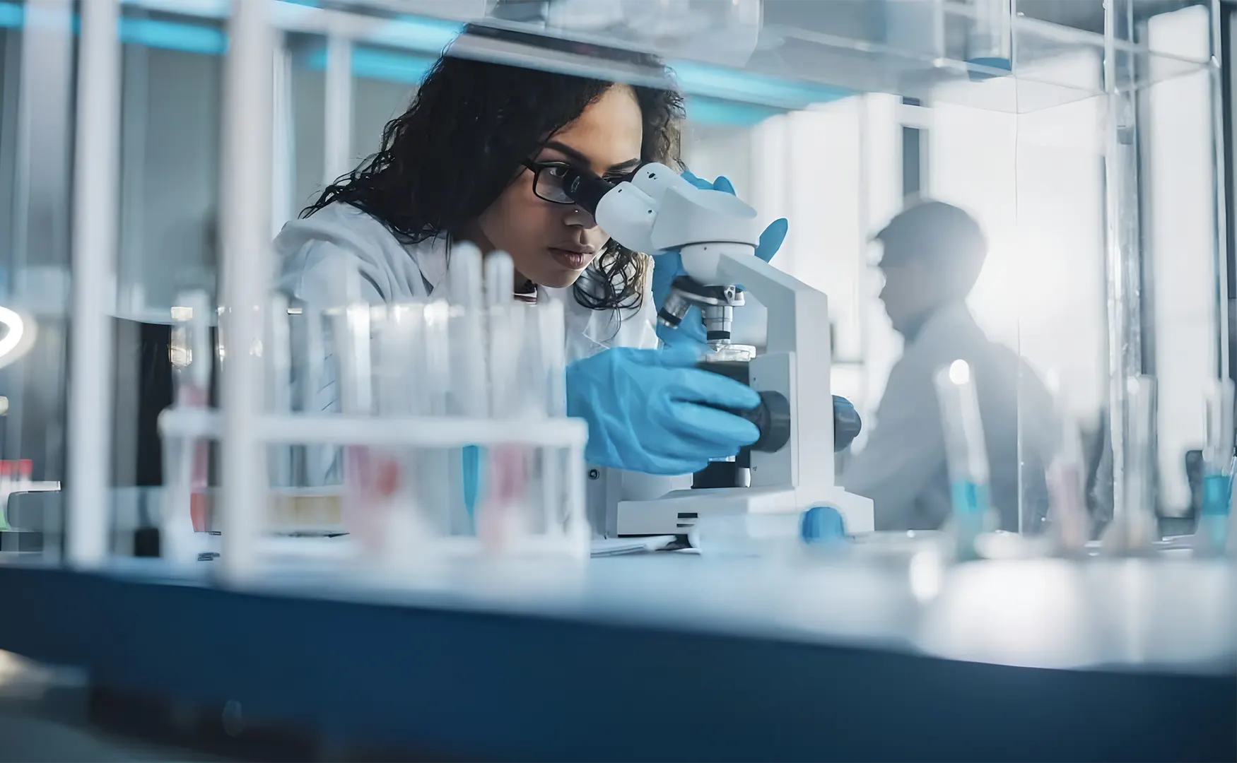Femme scientifique regardant dans un microscope avec des tubes à essai en avant-plan dans un laboratoire.