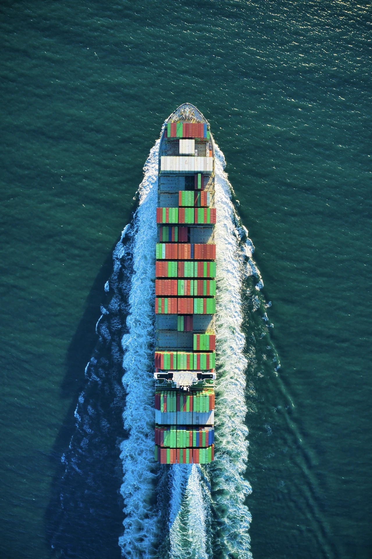 Vue aérienne d'un cargo transportant plusieurs conteneurs sur une mer bleue.
