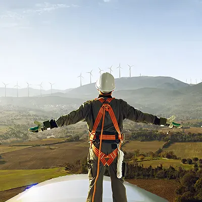 Person in safety gear standing on wind turbine overlooking a landscape with many wind turbines.