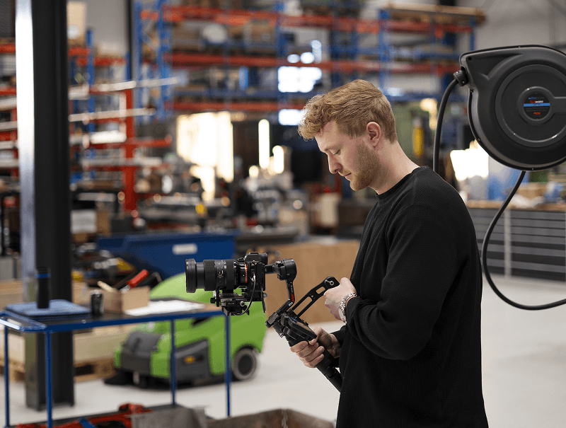 Mand i sort trøje indstiller kamera på gimbal i en industribygning.