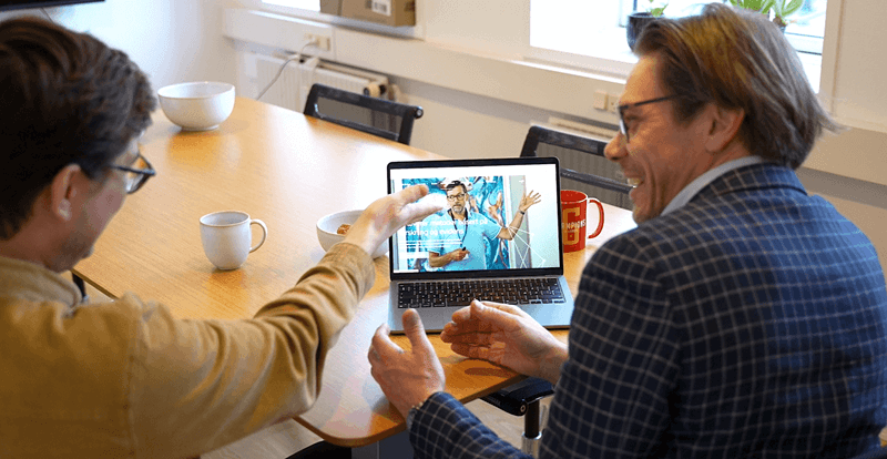 To mænd diskuterer og peger på en laptop med en ingeniør, der forklarer noget ved en vindmøllemodel.