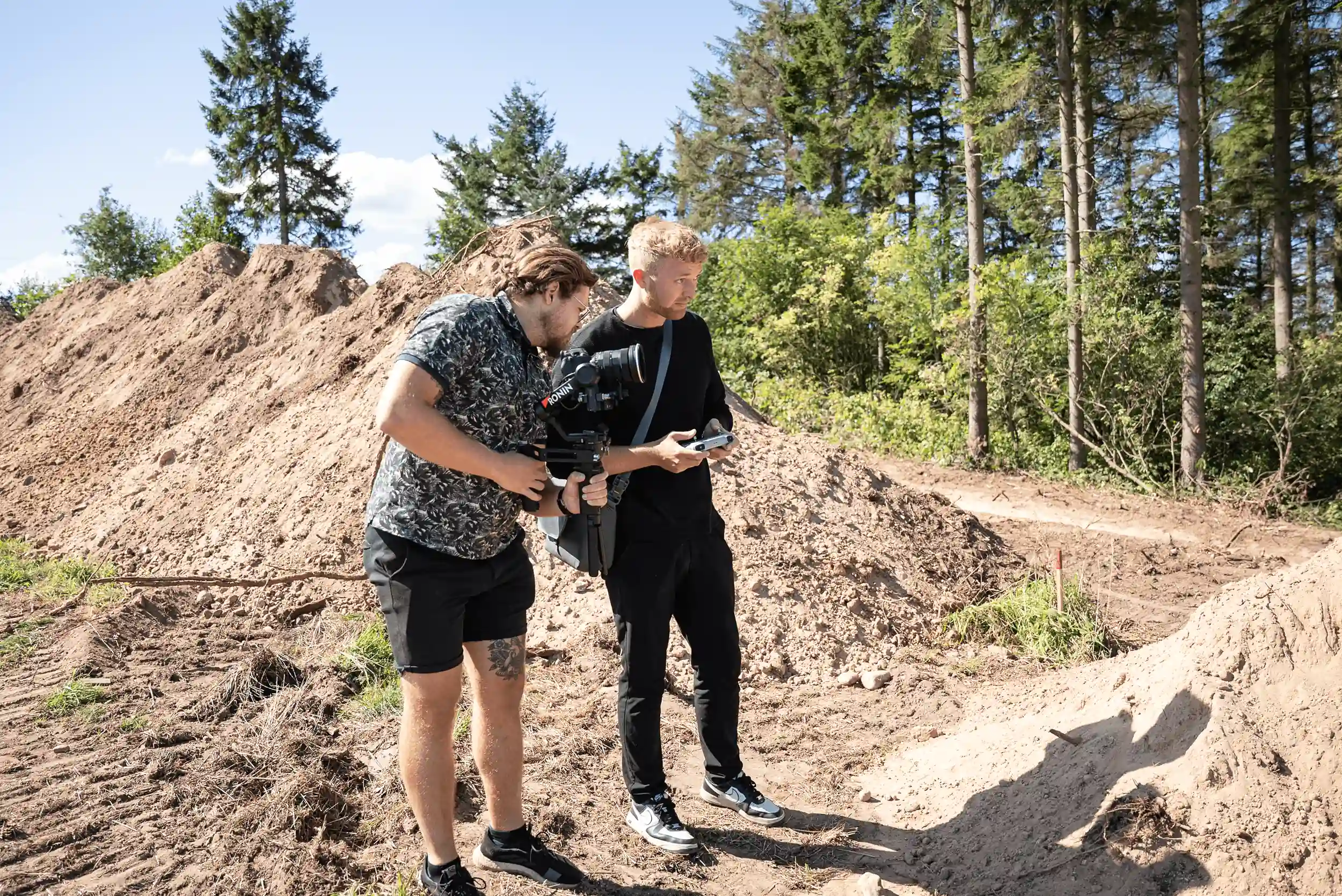 To mænd står i en skov, den ene med et kamera på en stabilisator og den anden med en fjernbetjening.