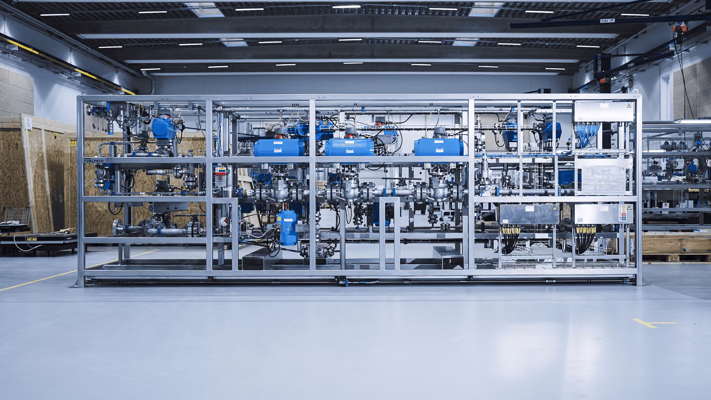 Industrielt anlæg med rør, ventiler og blå kontrolenheder i en fabrikshal.