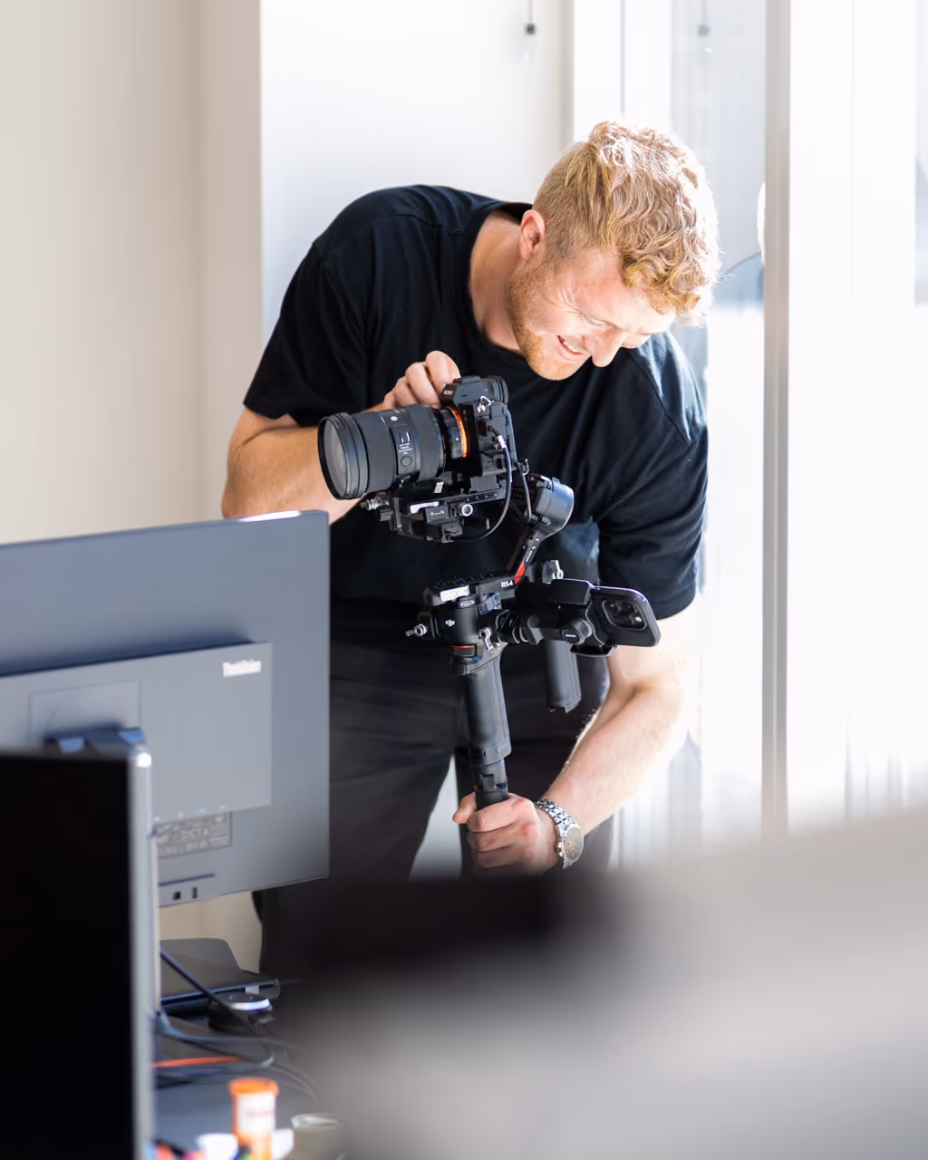 Mand med sort t-shirt justerer kamera på tredimensionel gimbal indendørs ved vindue.