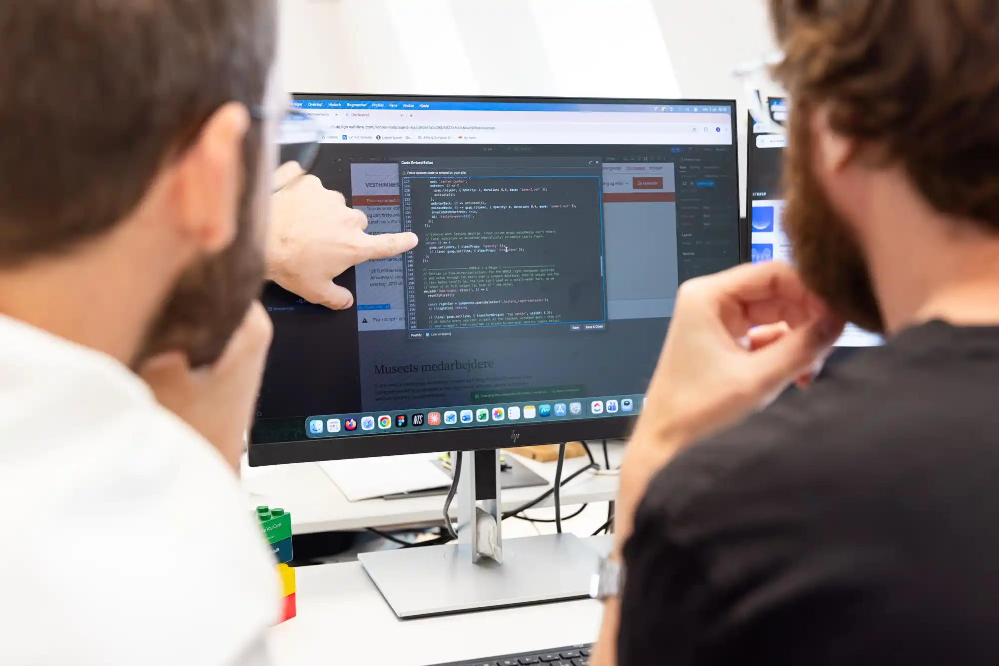 To mænd diskuterer kode på en computerskærm i et lyst kontormiljø.