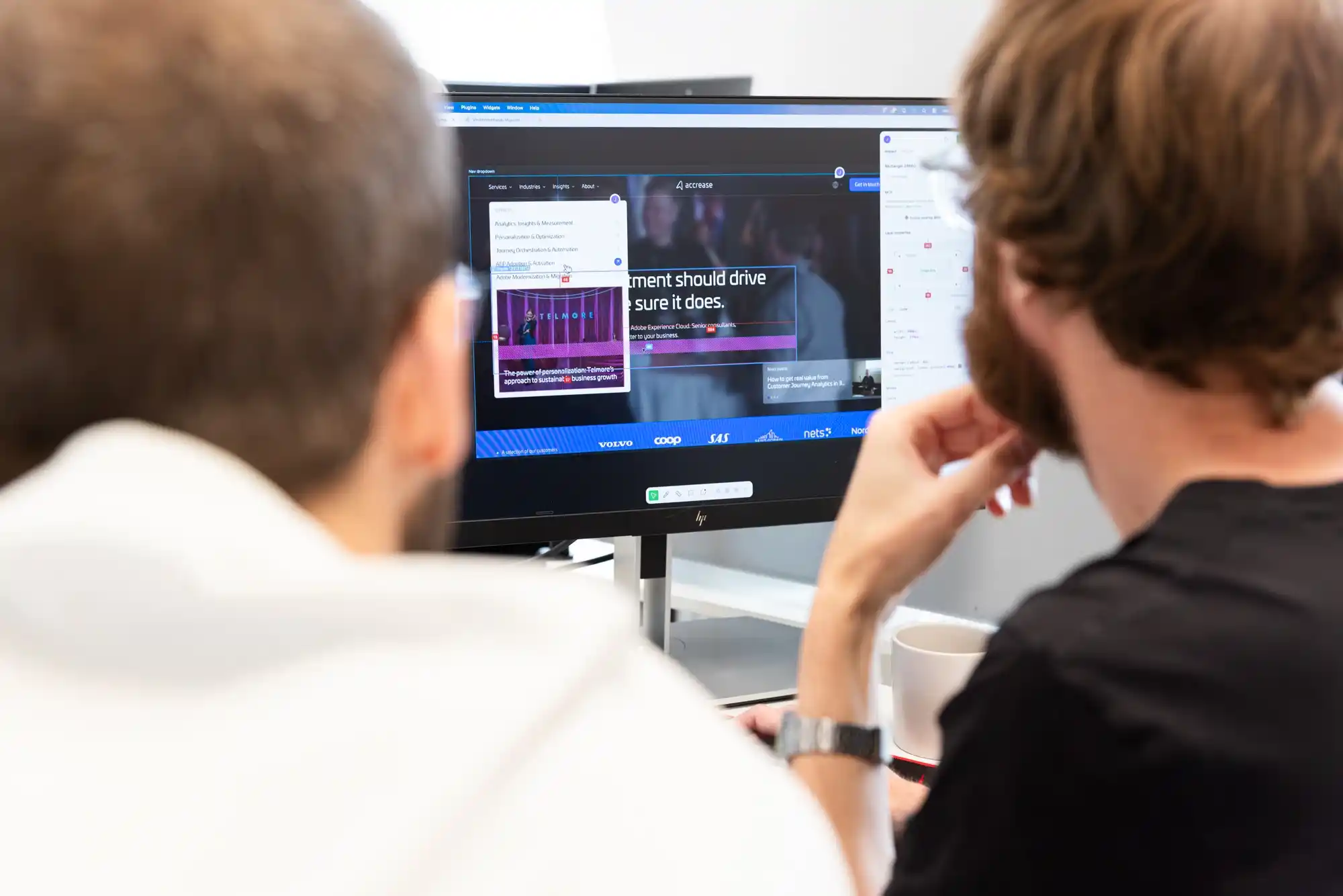 To mænd ser på en computerskærm, der viser en erhvervssoftwaregrænseflade med tekst og videoer.