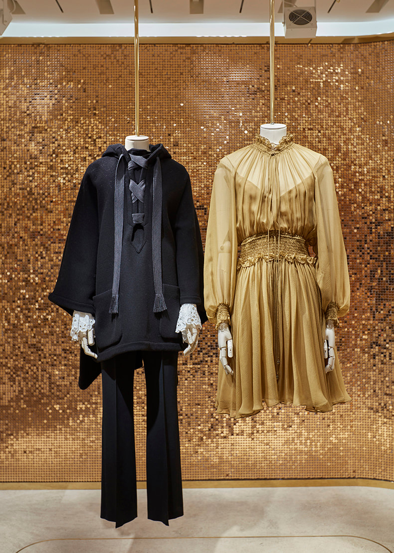 Two mannequins hovering in front of the gold sequin backdrop.