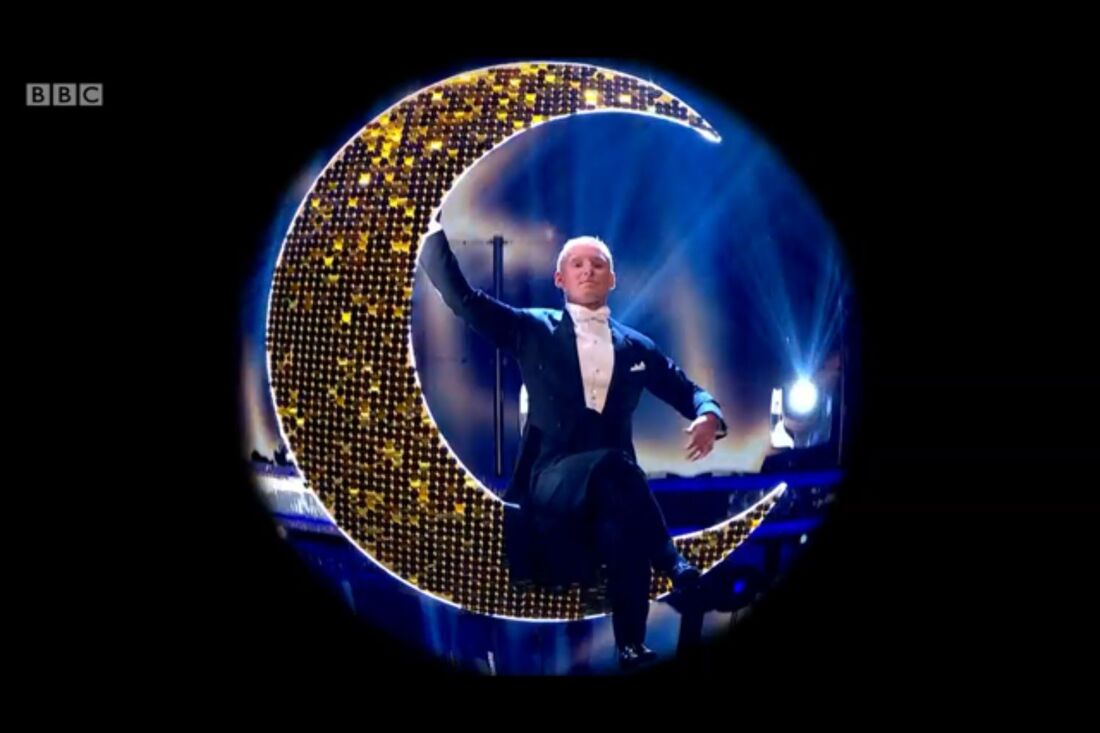 man in suit sitting on a gold crescent sequin moon