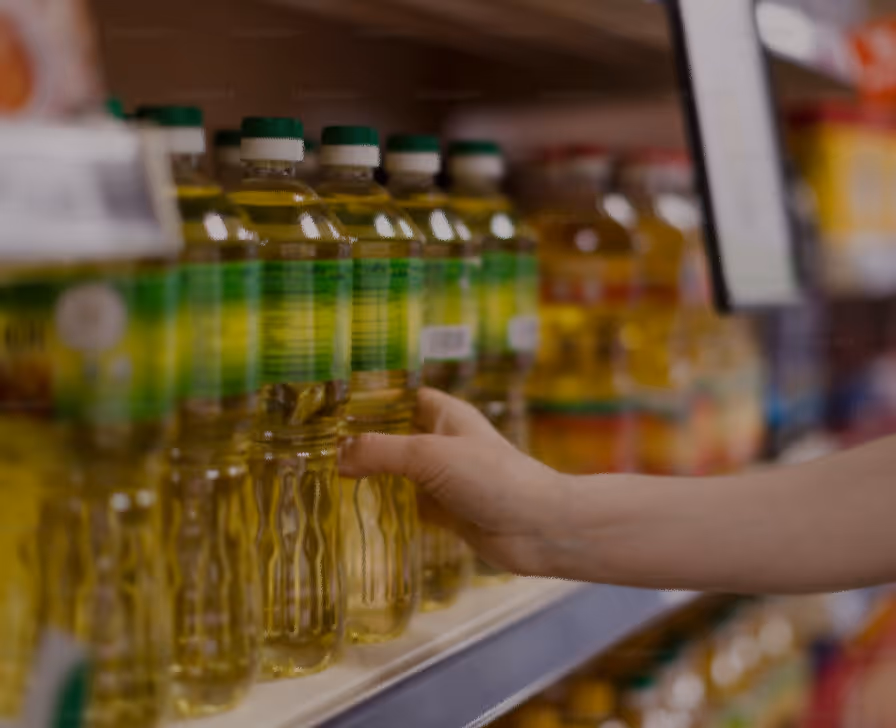 Hand reaching to pick a bottle of cooking oil from a grocery store shelf.