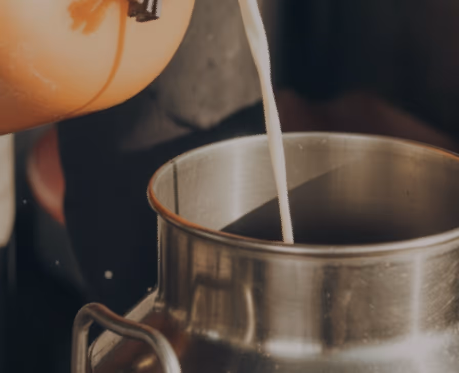 Milk being poured from an orange container into a stainless steel container.