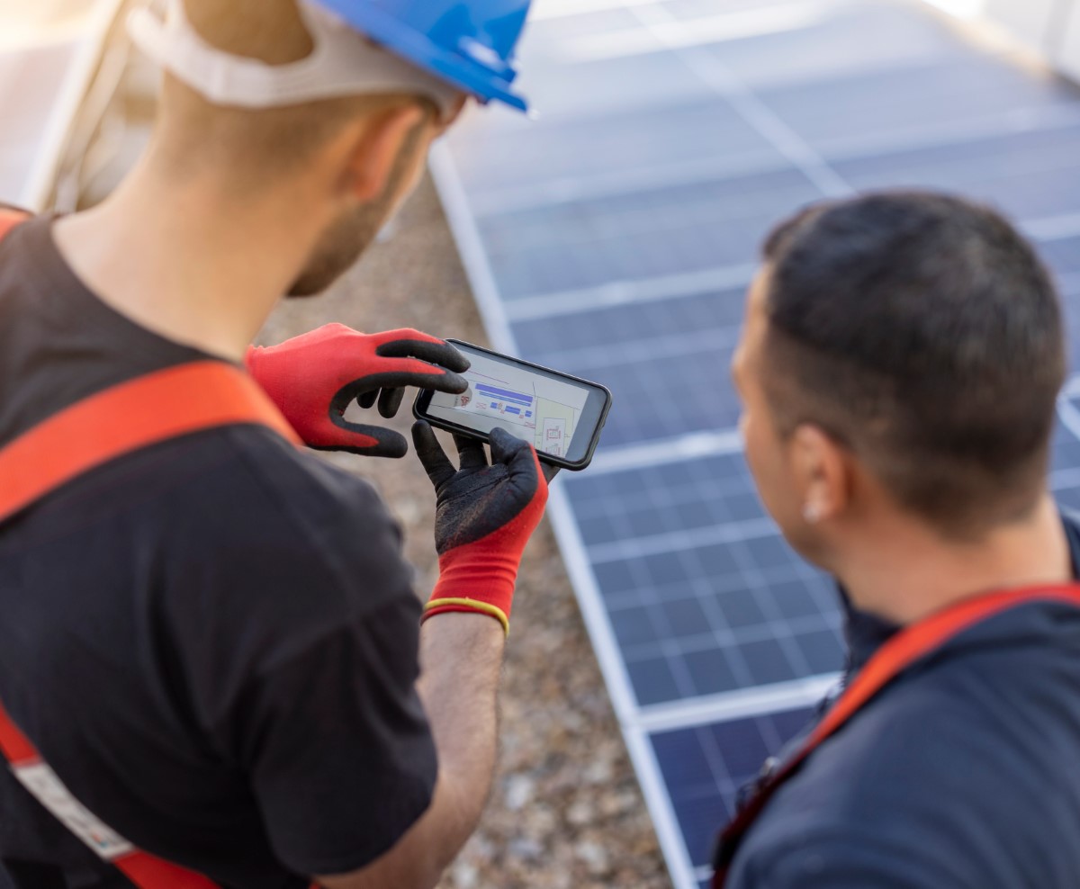 Technician in red gloves checking solar panel data on smartphone during installation