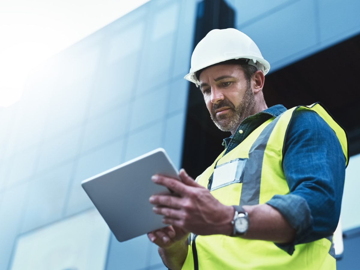 Construction worker in hard hat and safety vest using tablet at building site