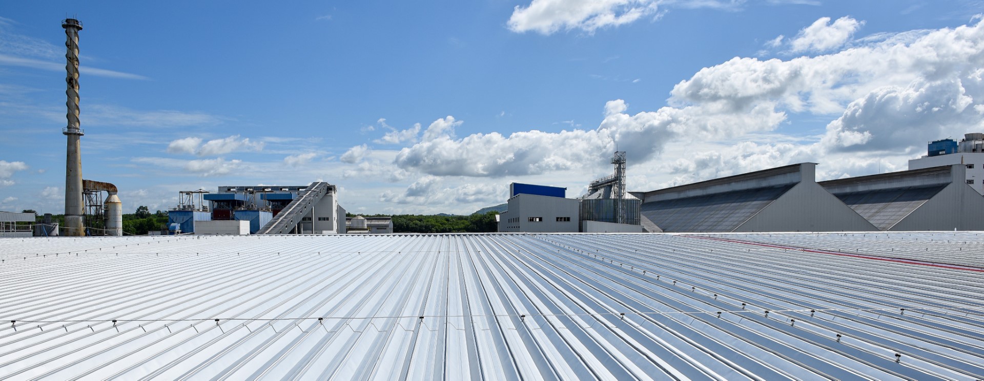 Industrial warehouse roof with metal corrugated panels and factory buildings against blue sky