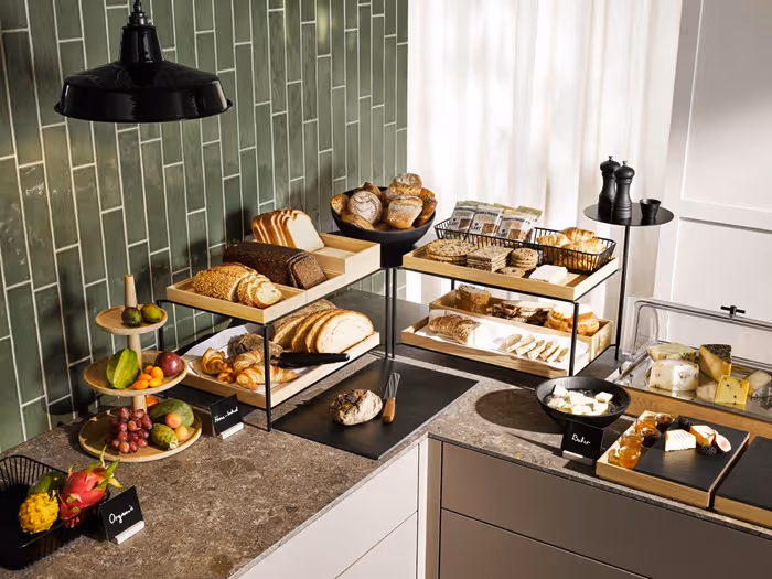 Buffet mit Brotauswahl, Käse, Früchten und Frühstücksspezialitäten auf mehrstöckigen Präsentationsflächen.