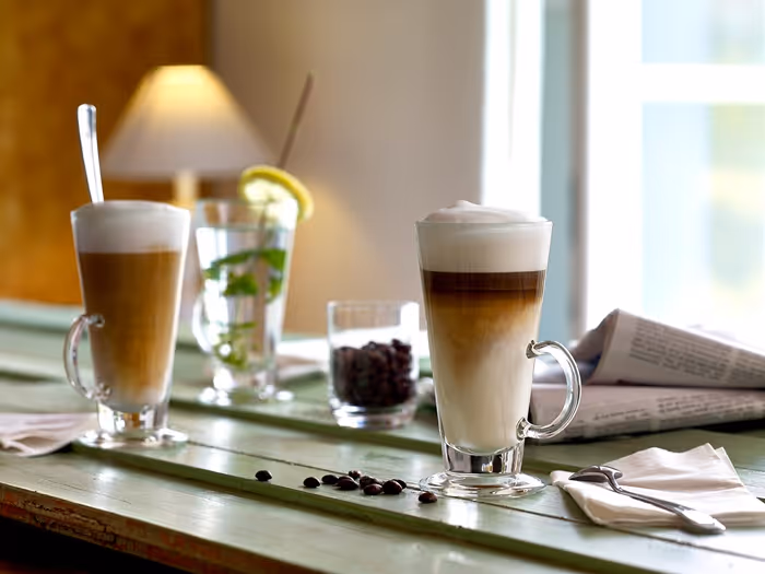 Latte Macchiato und Kaffeegetränke in Glasbechern auf einem gedeckten Tisch im Café.