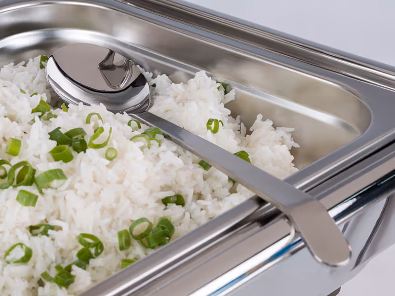 Edelstahlbehälter mit Reis, Frühlingszwiebeln und Servierlöffel für die Speisenausgabe am Buffet.