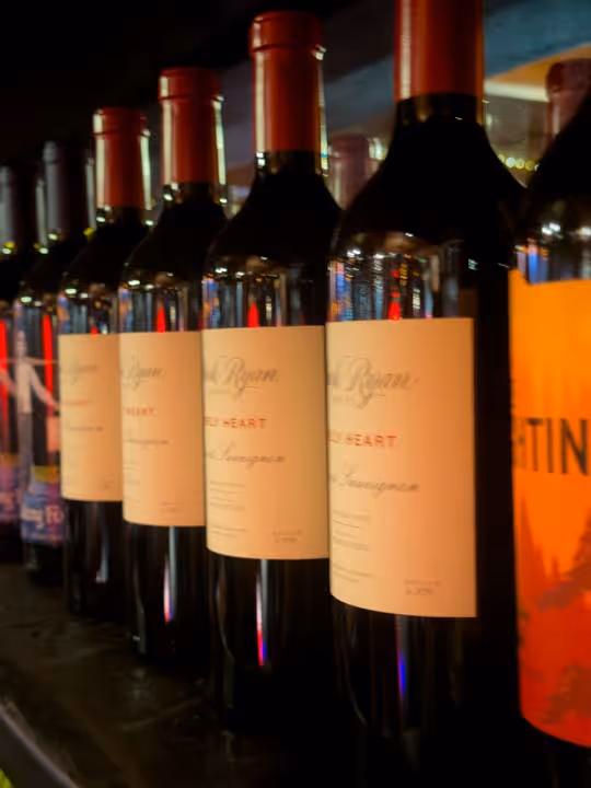 Row of wine bottles with red foil tops and cream labels lined up on a shelf.