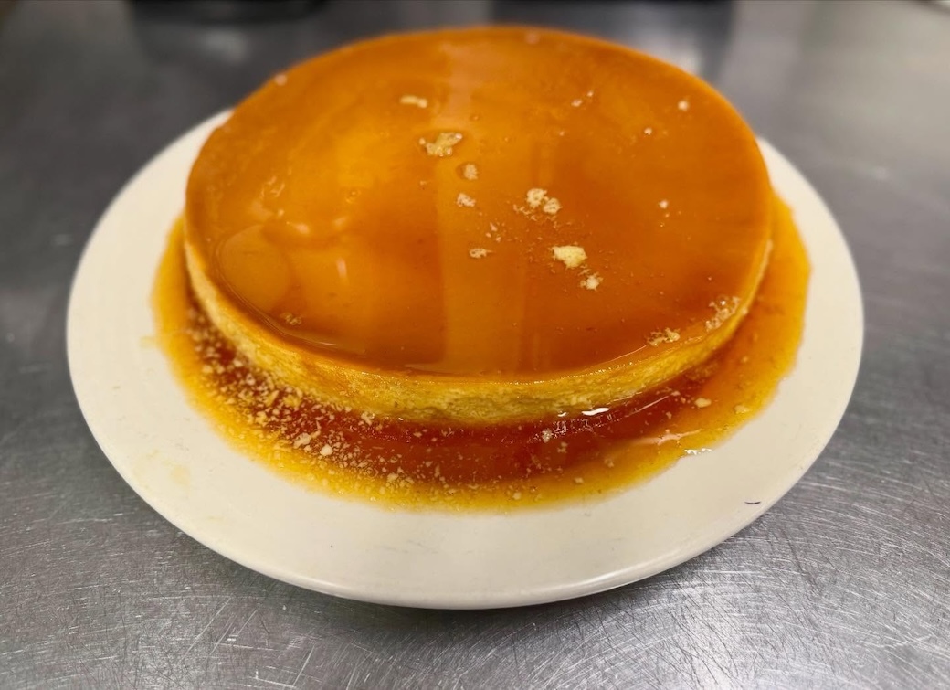 Caramel flan dessert on a white plate with caramel sauce spilling over the edges.