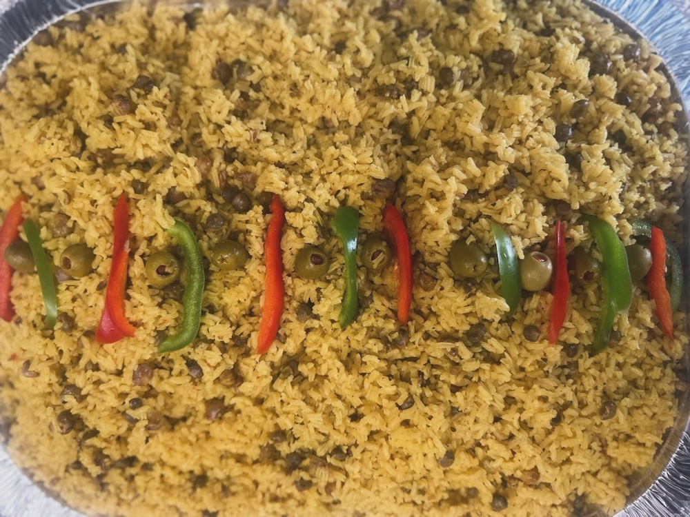 Tray of seasoned rice with black beans, garnished with a row of green olives and alternating red and green bell pepper strips.