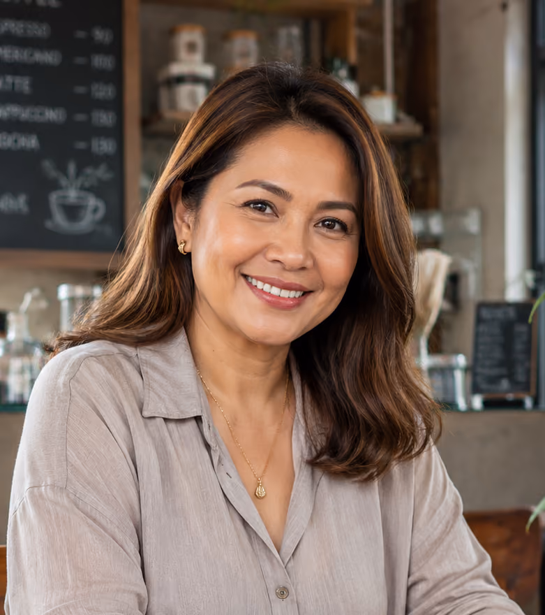 Smiling woman with medium-length brown hair wearing a beige blouse in a cozy cafe setting.
