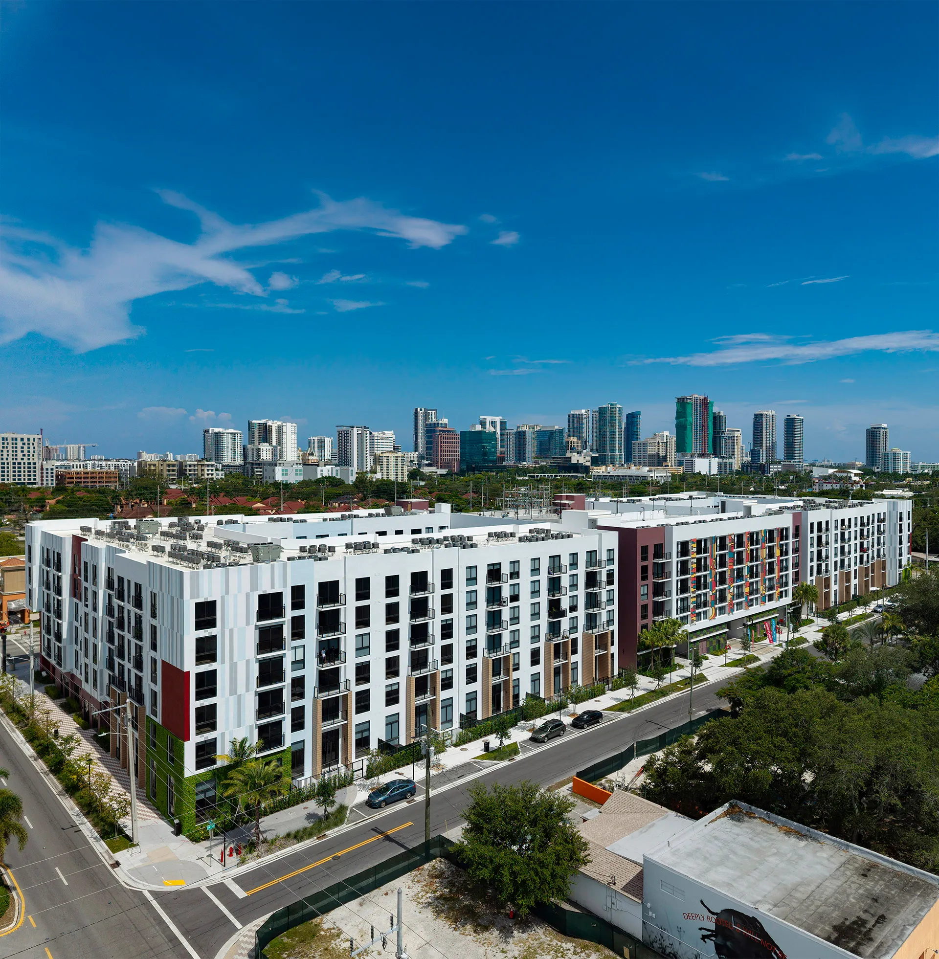 Modern apartment complex with multiple stories near a city skyline under a clear blue sky.