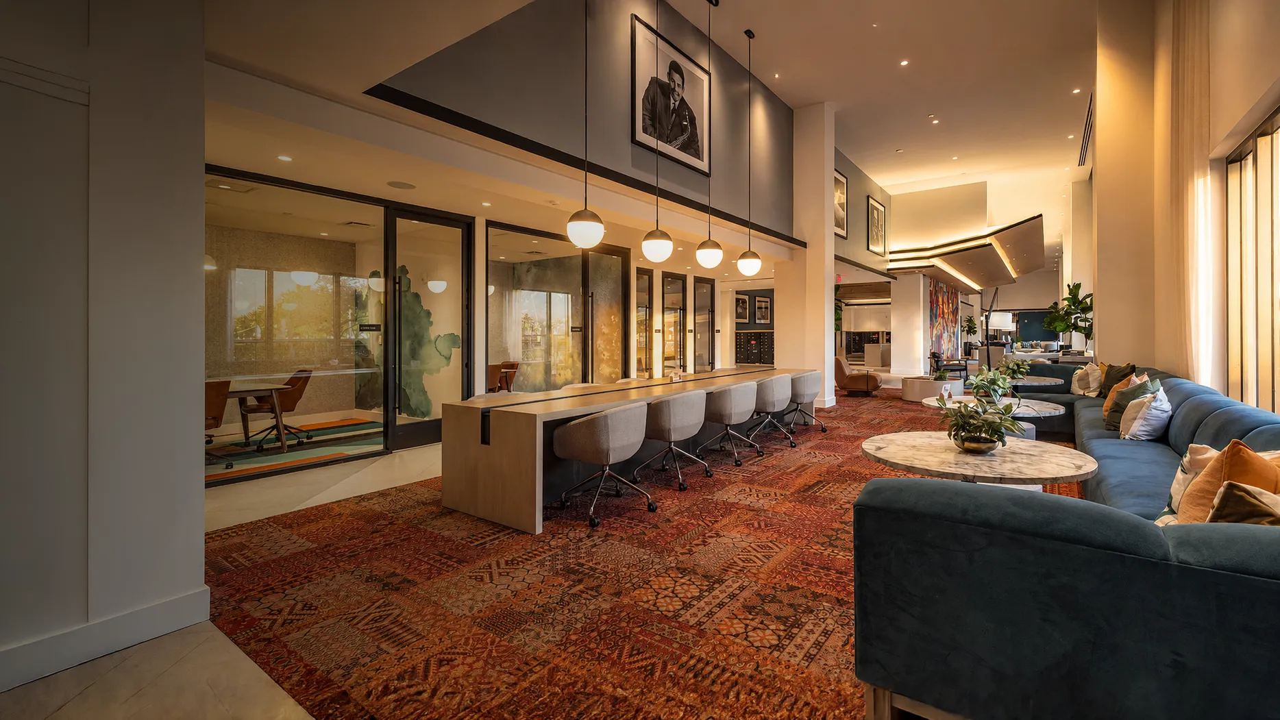 Modern lounge with blue sofas, round marble tables, patterned carpet, and a work area with chairs.