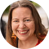 Smiling woman with curly brown hair and red lipstick wearing a red top and white earrings.