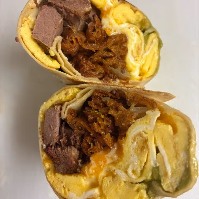 Close-up of two halves of a breakfast burrito filled with scrambled eggs, beef slices, and crispy hash browns.