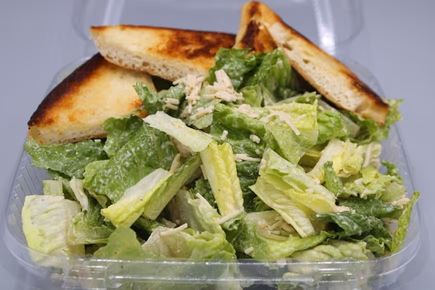Caesar salad with romaine lettuce, grated cheese, and three pieces of toasted bread in a clear plastic container.