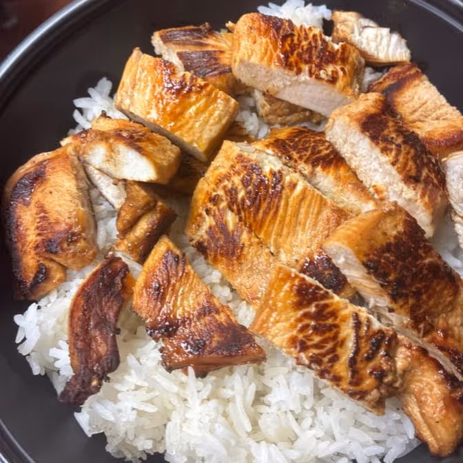 Grilled, sliced chicken served on a bed of white rice in a black bowl.