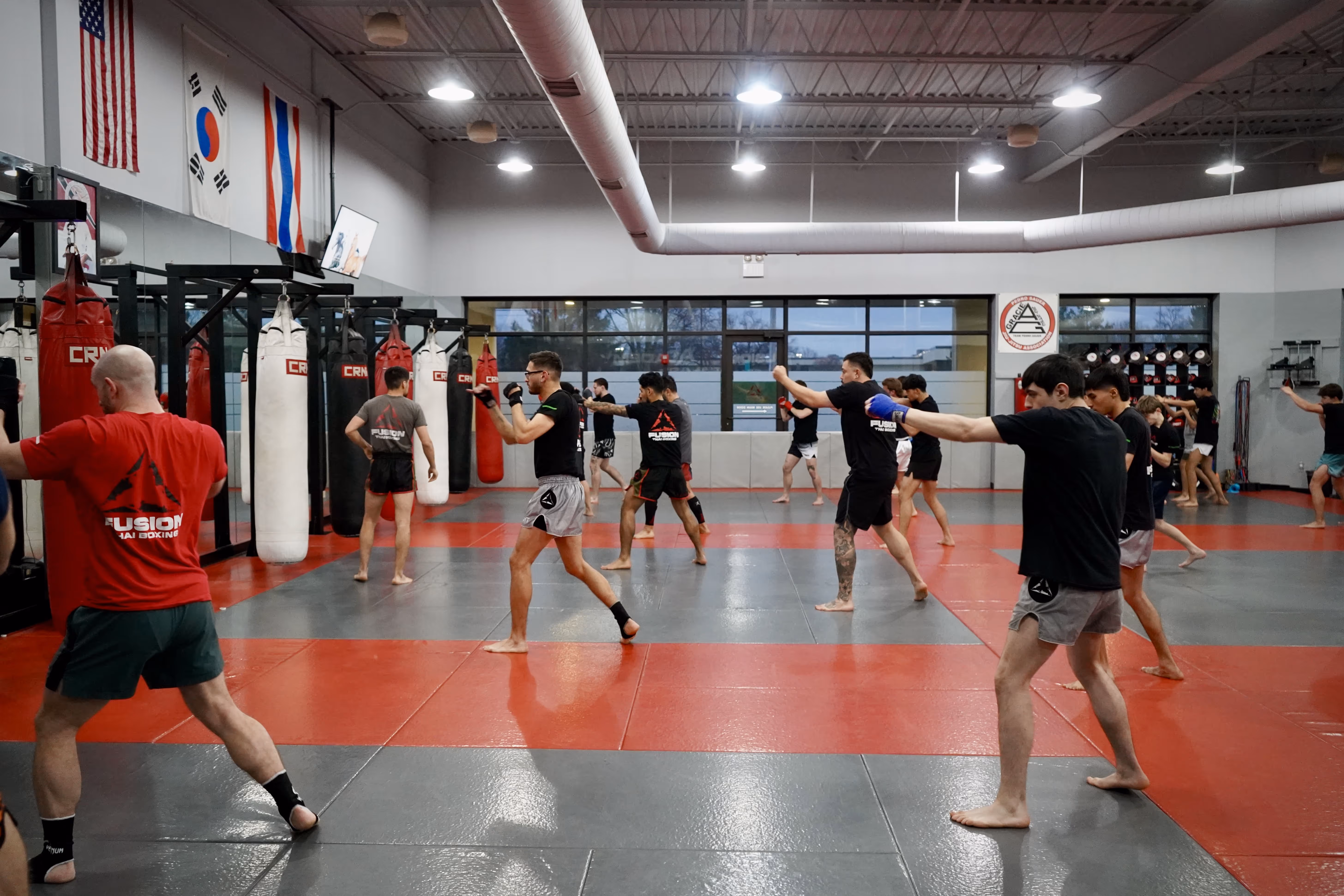 Group of people practicing martial arts punches in a gym with red and gray mats and punching bags.