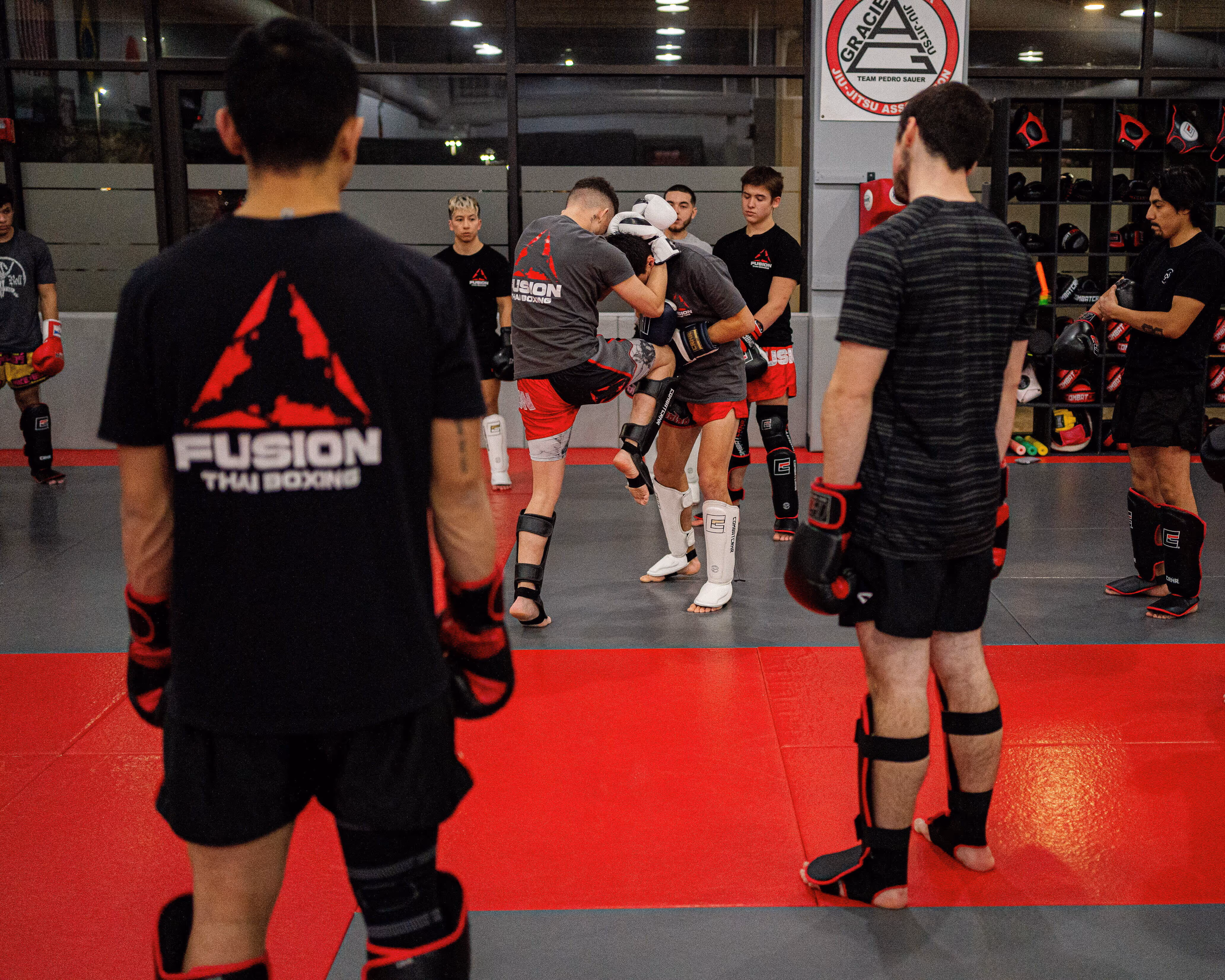 Martial arts class with fighters wearing gear practicing Muay Thai knee strikes in a gym.