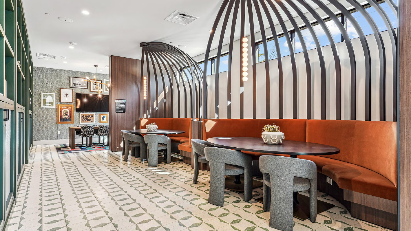Modern lounge area with curved orange booths, gray chairs, and a geometric tiled floor under skylights.