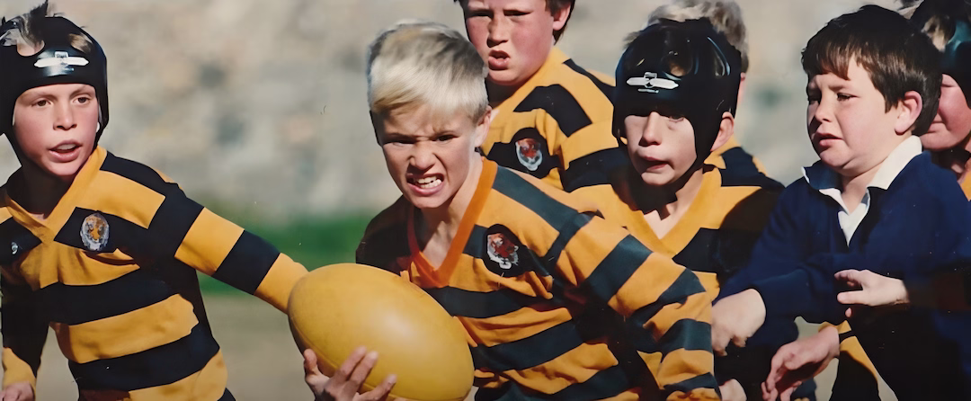 Young boys in striped rugby uniforms playing a game, one holding a rugby ball tightly.