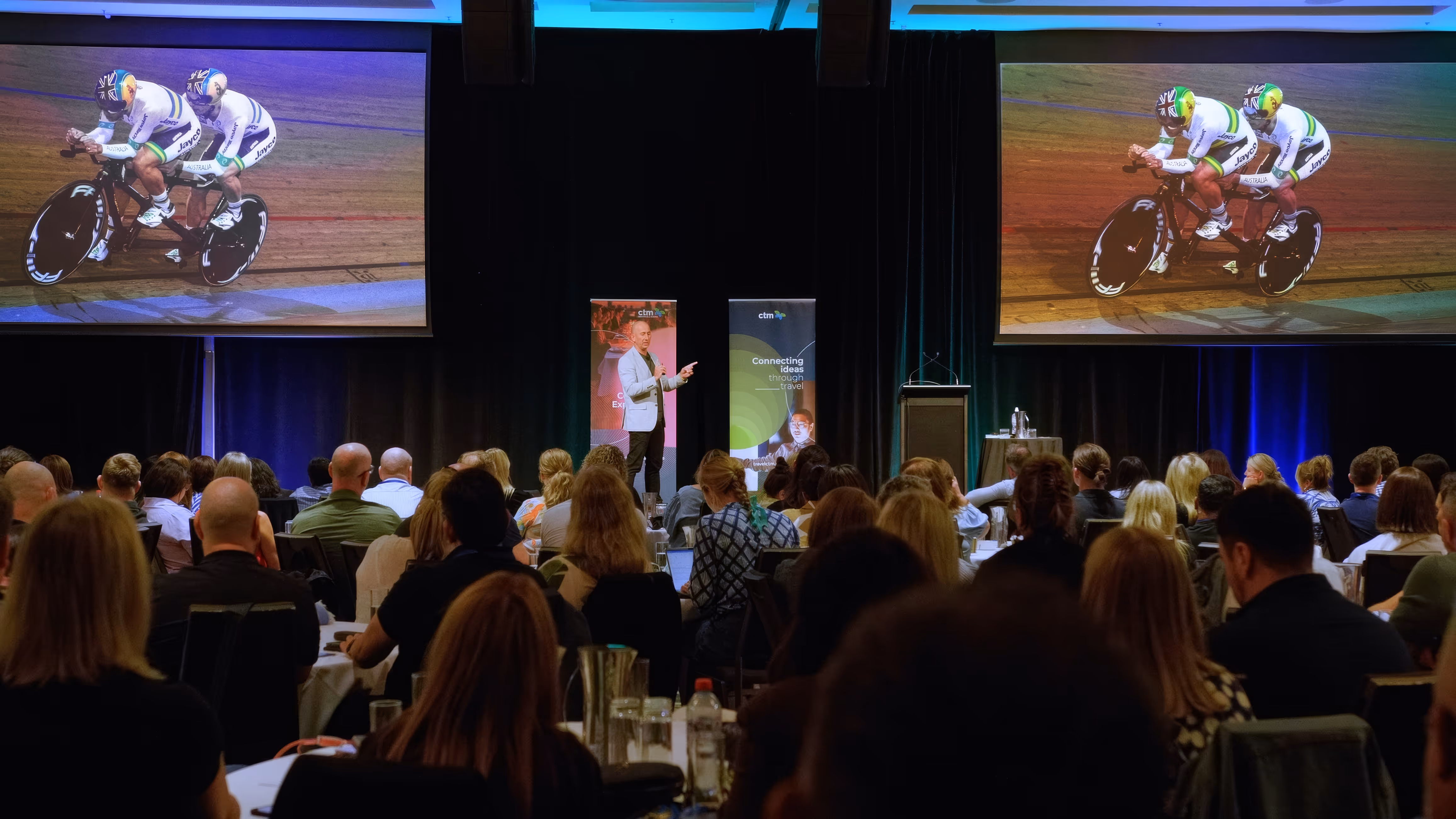 Man in suit speaking on stage at ANZ Enterprise Connect 2019 conference with geometric blue backdrop.