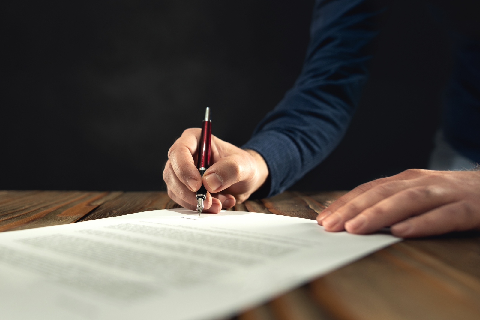 Hand signing a contract document — direct ownership vs passive investment vehicles