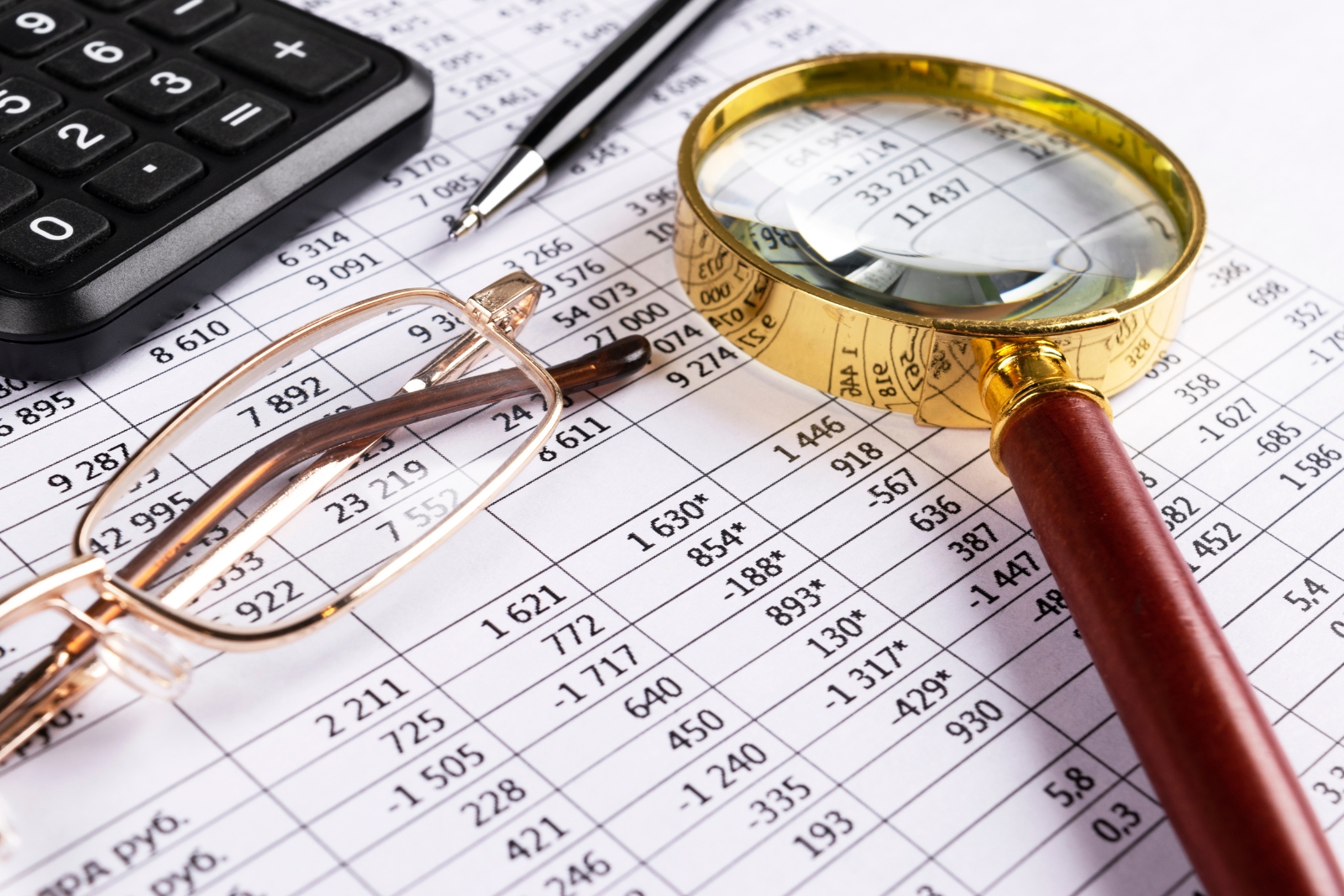 Magnifying glass and calculator over financial spreadsheet — risks operating statements don't show