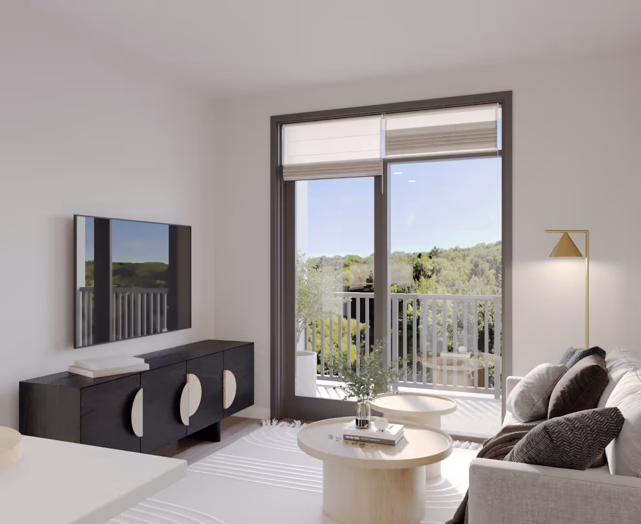 Modern living room with a gray sofa, decorative pillows, round wooden coffee tables, a wall-mounted TV, and glass door leading to a balcony with greenery outside.