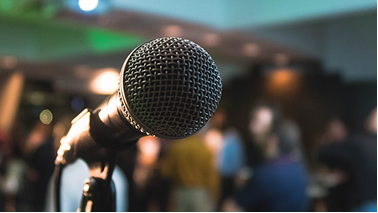 Close-up of a microphone in front of a blurred crowd at an indoor event.