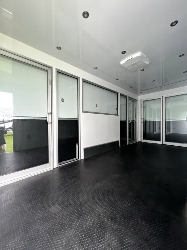 Marketing kiosk with black rubber flooring, white walls, large windows, glass doors, and ceiling air conditioning unit.