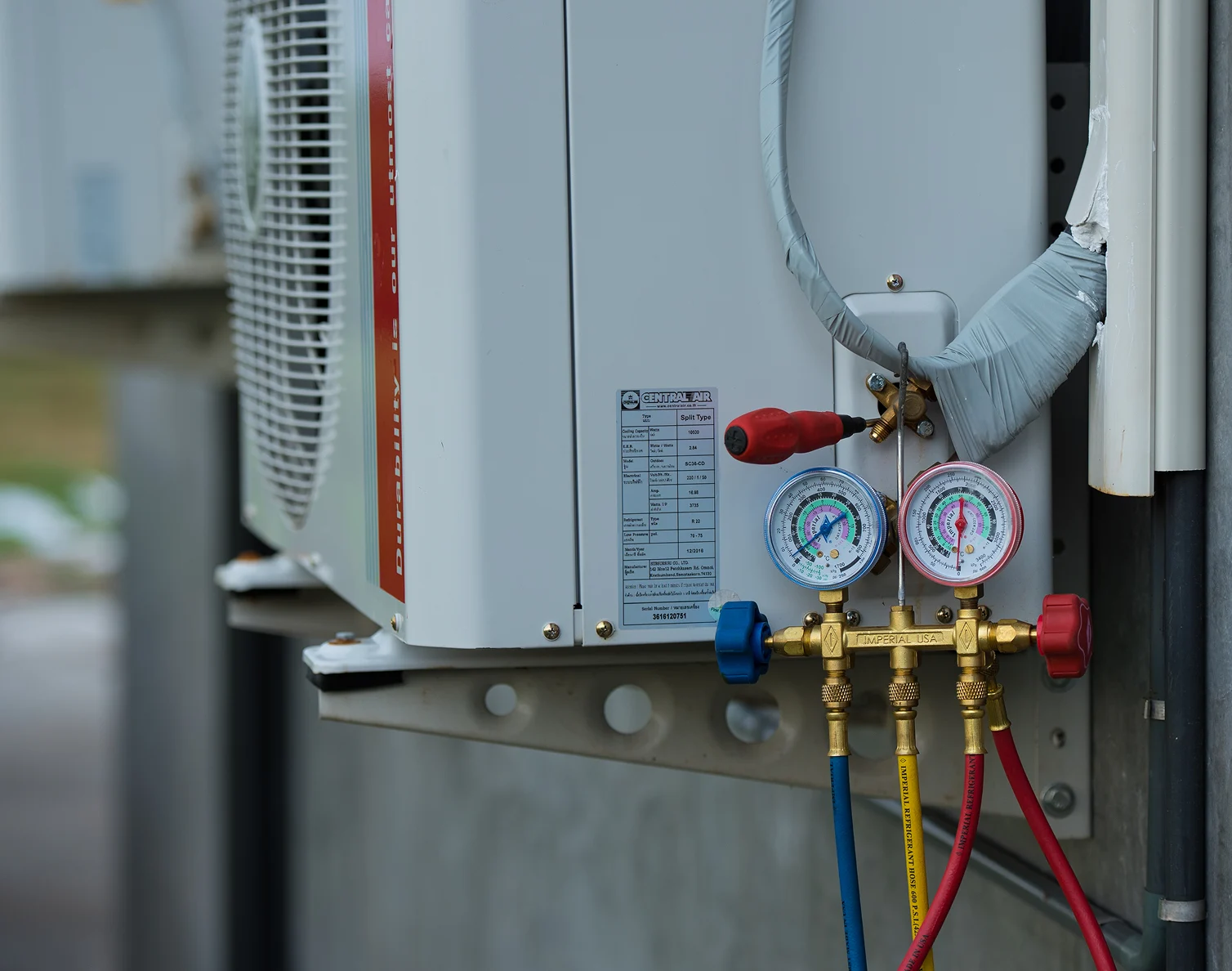 Close-up of HVAC unit with pressure gauges and red, yellow, and blue hoses connected for maintenance.